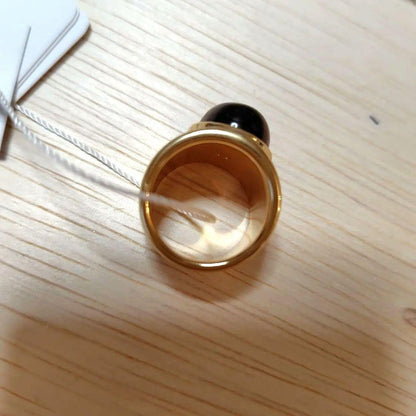 A gold ring with a spherical design featuring onyx and tiger's eye stones.